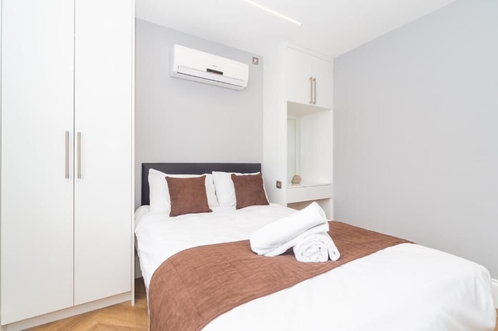 A hotel room with a bed, white wardrobe, and a wall-mounted air conditioning unit.