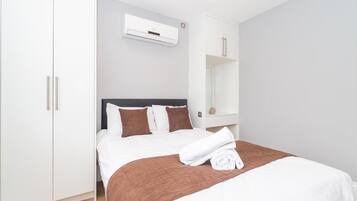 A hotel room with a bed, white wardrobe, and a wall-mounted air conditioning unit.