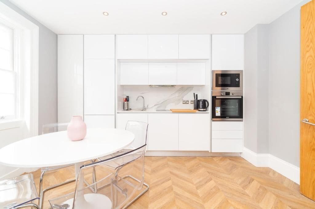 Een moderne keuken met witte kasten, een ronde witte tafel met stoelen en een visgraat houten vloer.