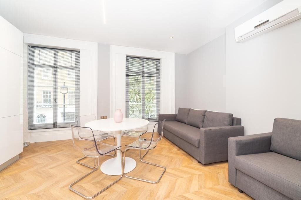 A modern living room with a round table, two grey sofas, and a large window with blinds.