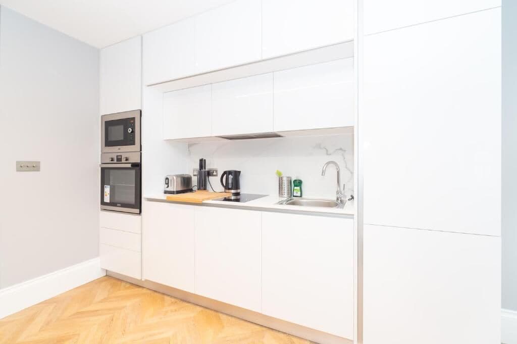 A modern kitchen with white cabinetry, a built-in microwave, a coffee maker, and a sink.