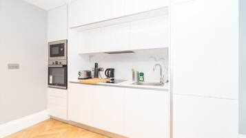 A modern kitchen with white cabinetry, a built-in microwave, a coffee maker, and a sink.