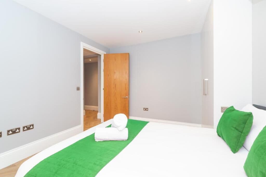 Un dormitorio con una cama, una alfombra verde, una puerta de madera y una pared blanca.