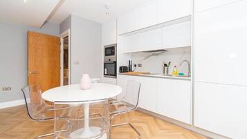 A modern kitchen with white cabinets, a round white table with chairs, and a wooden door.