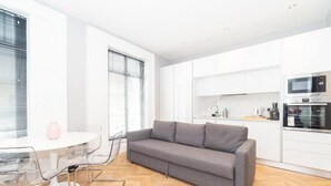 Una cocina moderna con armarios blancos, un sofá gris y un comedor con mesa y sillas blancas.