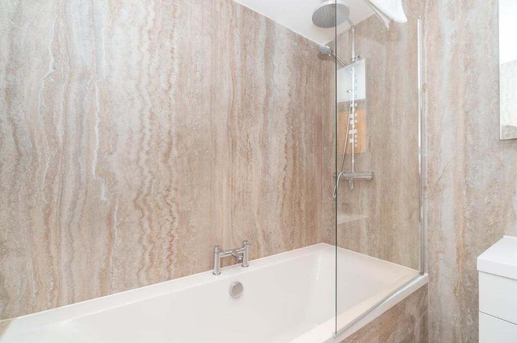 A modern bathroom with a glass-enclosed shower, a white bathtub, and marble walls.