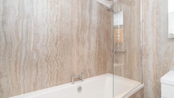 A modern bathroom with a glass-enclosed shower, a white bathtub, and marble walls.