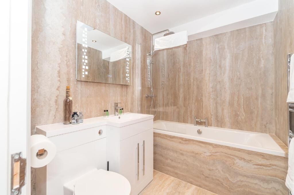 A bathroom with a marble wall, a white sink, a toilet, and a bathtub.