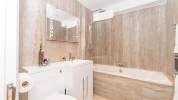 A bathroom with a marble wall, a white sink, a toilet, and a bathtub.