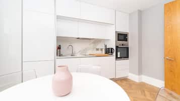 Una cocina moderna con gabinetes blancos, encimera de mármol y electrodomésticos de acero inoxidable.