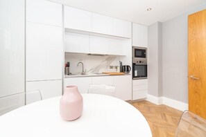 Una cocina moderna con gabinetes blancos, encimera de mármol y electrodomésticos de acero inoxidable.