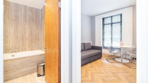 Un baño moderno con bañera y ducha, un sofá gris, y un comedor con mesa y sillas.