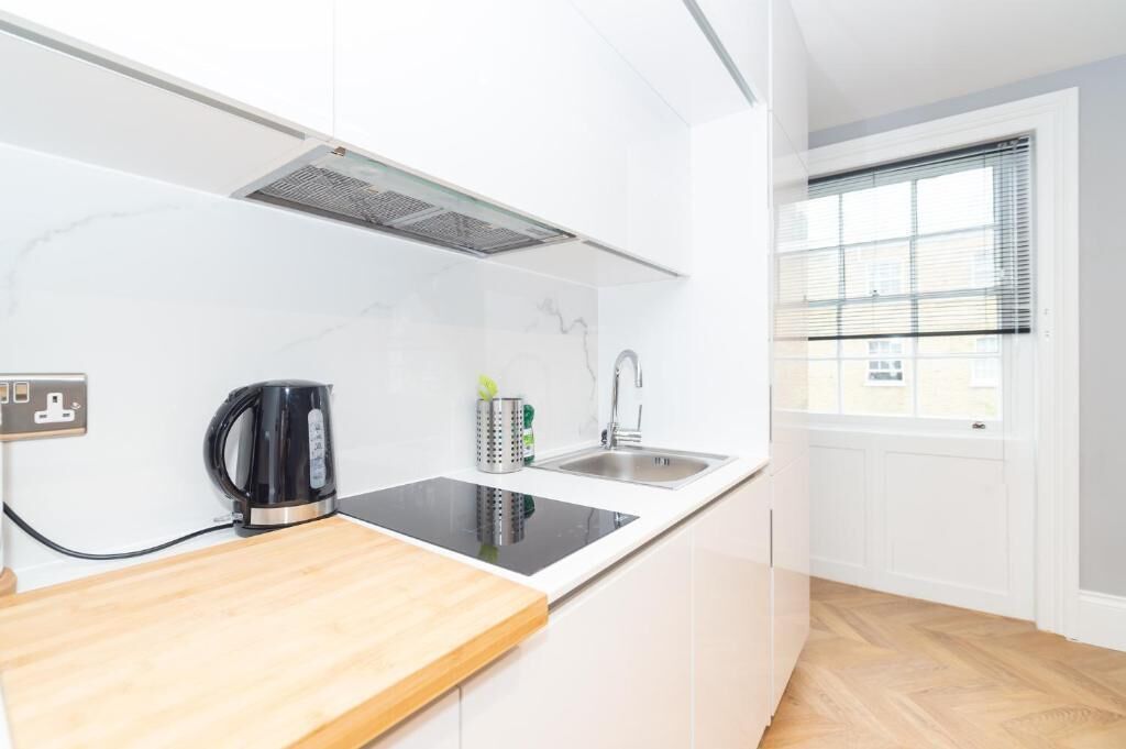 Una cocina moderna con una placa de inducción negra, un lavamanos de acero inoxidable y una ventana con persianas.