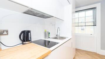 Una cocina moderna con una placa de inducción negra, un lavamanos de acero inoxidable y una ventana con persianas.