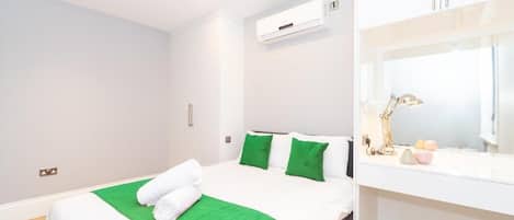Una habitación de hotel con una cama, ropa de cama verde y blanca, una lámpara de noche y una mesita de noche pequeña con una lámpara y algunos objetos.