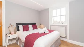 A neatly arranged bedroom with a bed, bedside table, lamp, and window.