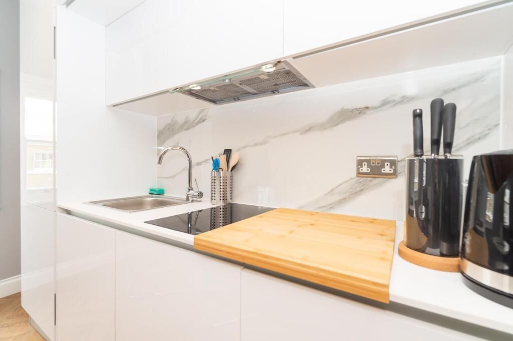 A modern kitchen with white cabinetry, a black induction cooktop, a wooden cutting board, a sink, and a knife block.
