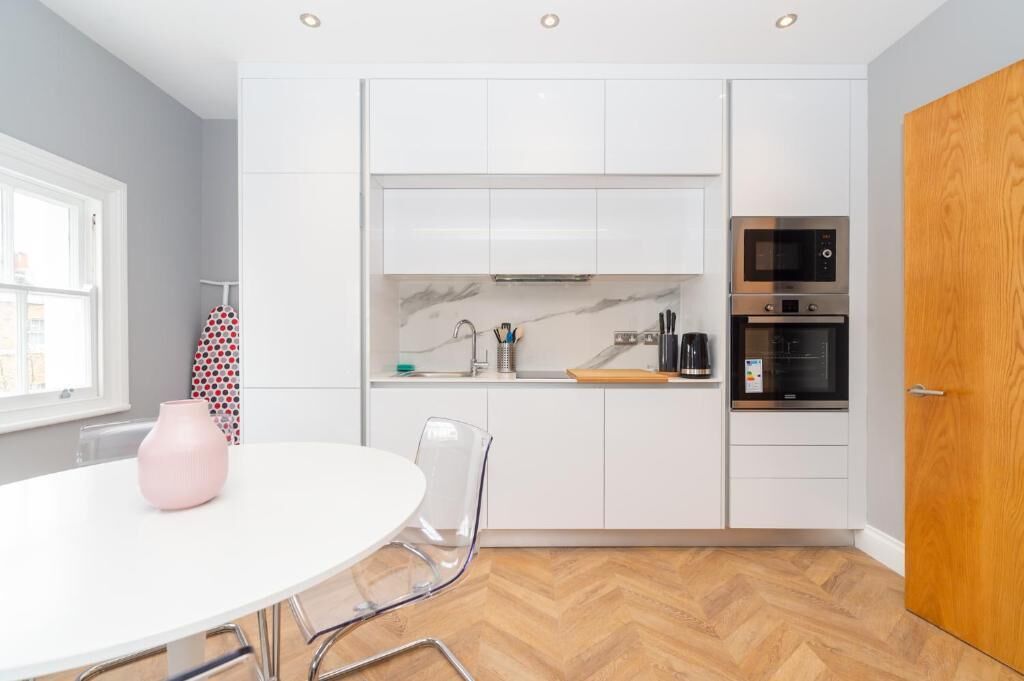 Une cuisine moderne avec des meubles blancs, un four à micro-ondes, un four traditionnel et un coin repas comprenant une table et des chaises blanches.
