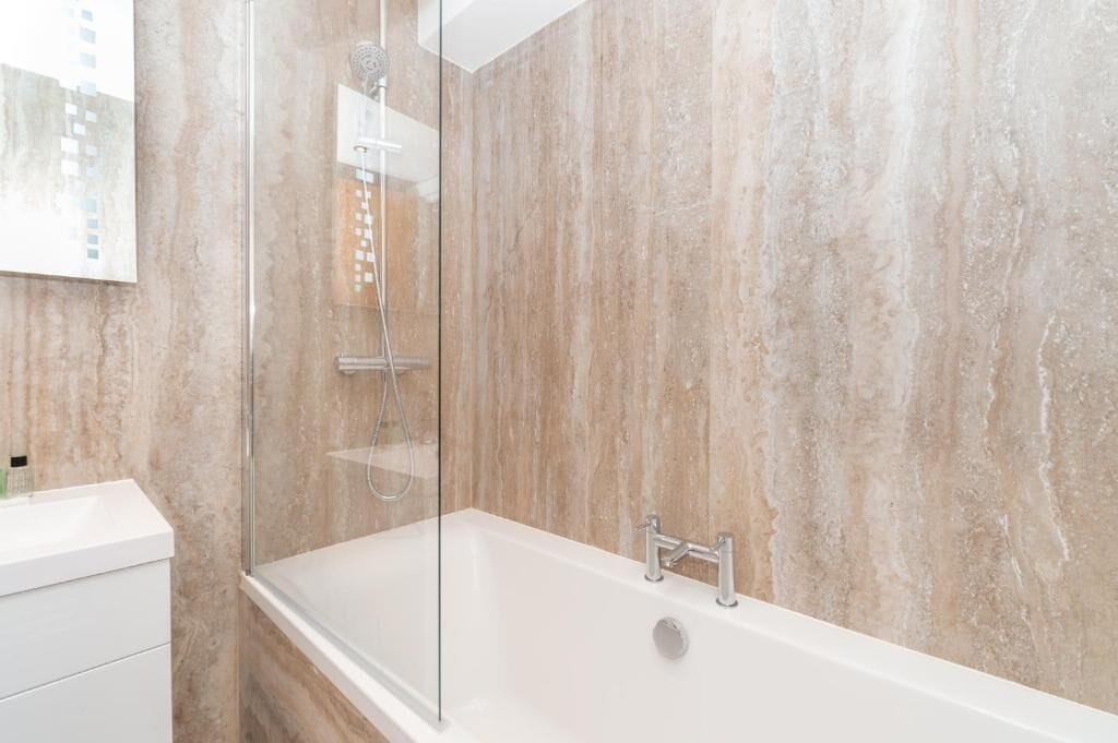 A modern bathroom with a glass-enclosed shower, a white bathtub, and marble walls.