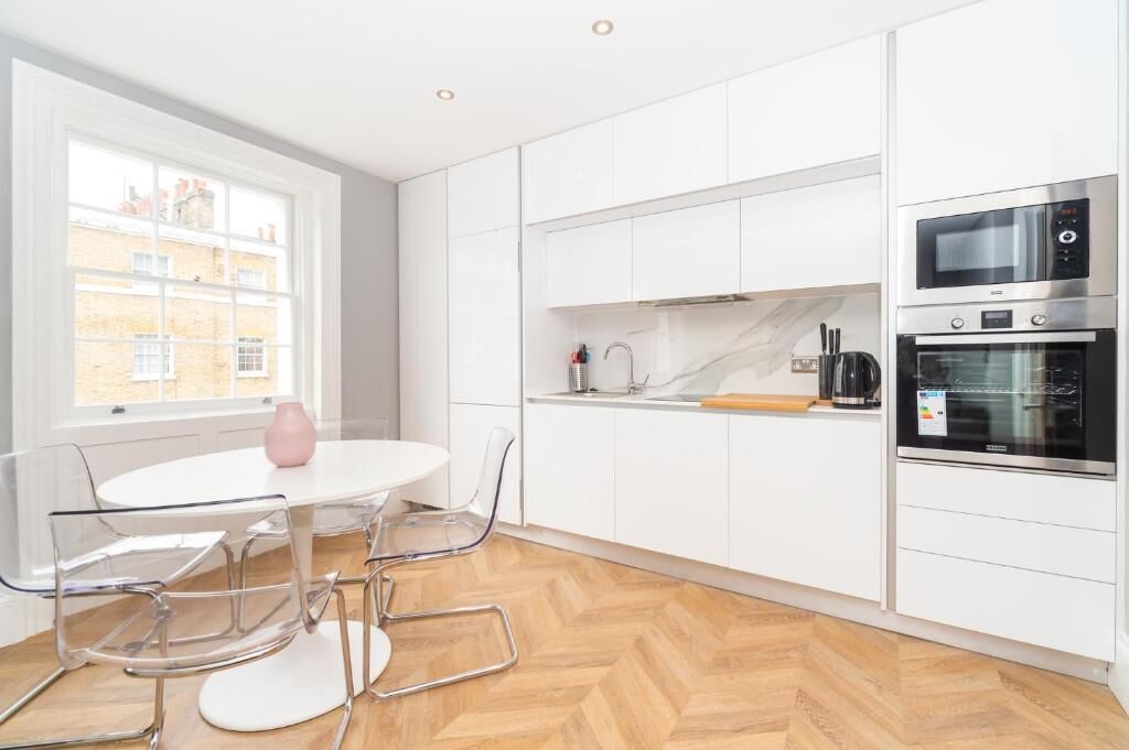 Una cocina moderna con armarios blancos, horno empotrado y comedor con una mesa redonda y sillas.