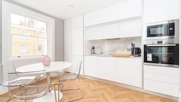 Una cocina moderna con armarios blancos, horno empotrado y comedor con una mesa redonda y sillas.