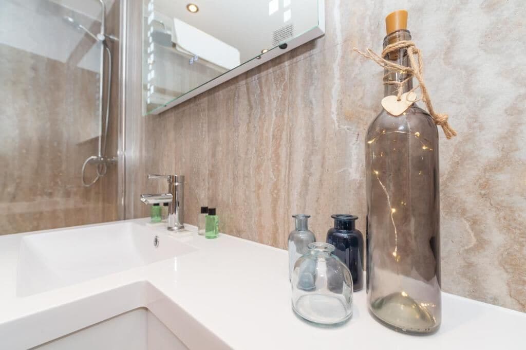 Un baño con un lavamanos blanco, una botella de vidrio con tapón de corcho y varios recipientes pequeños de vidrio sobre la encimera.