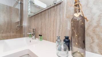 Un baño con un lavamanos blanco, una botella de vidrio con tapón de corcho y varios recipientes pequeños de vidrio sobre la encimera.