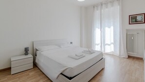 Quarto minimalista com uma cama de solteiro, mesa de cabeceira e um radiador.
