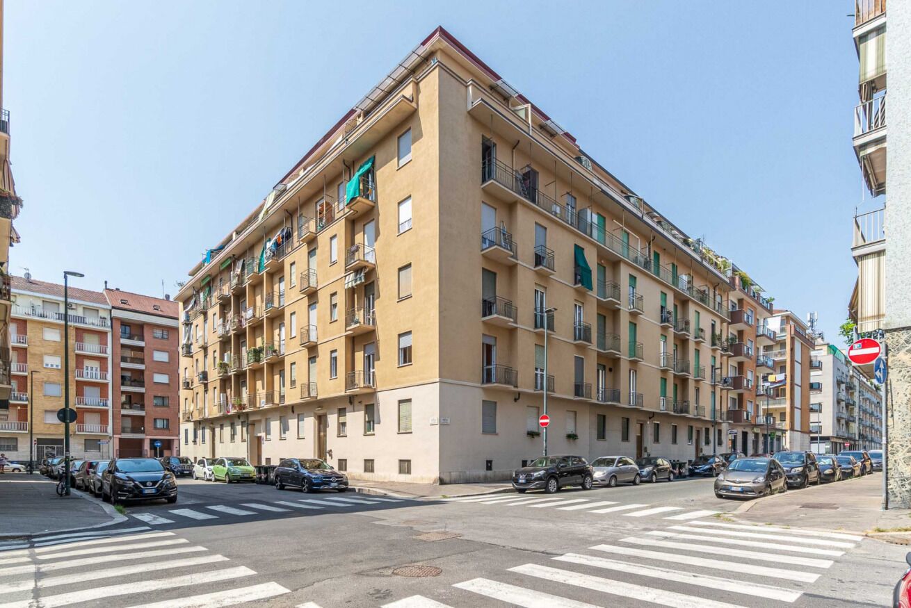 Un edificio residencial de varios pisos con balcones, un paso de peatones y coches estacionados.