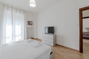 A hotel room with a bed, a TV on a dresser, a radiator, and a window with curtains. - A bright and comfortable 48 square meters apartment, perfect for three people, located on the third floor of a renovated building with an elevator (NOT accessible to people with disabilities).The property is situated in an extremely quiet area well-serve (Turin)