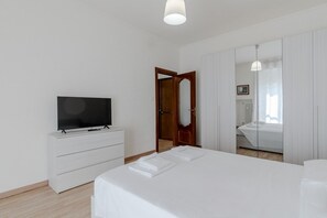 A bedroom with a bed, a television on a dresser, a mirror, and a door leading to another room. - A bright and comfortable 48 square meters apartment, perfect for three people, located on the third floor of a renovated building with an elevator (NOT accessible to people with disabilities).The property is situated in an extremely quiet area well-serve (Turin)