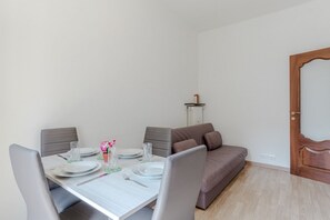 A dining area with a table set for two, a grey sofa, and a wooden door. - A bright and comfortable 48 square meters apartment, perfect for three people, located on the third floor of a renovated building with an elevator (NOT accessible to people with disabilities).The property is situated in an extremely quiet area well-serve (Turin)