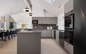 A modern kitchen with a central island, black appliances, and a dining area with chairs and a vase. - Nice home in Otterup with WiFi (Otterup)