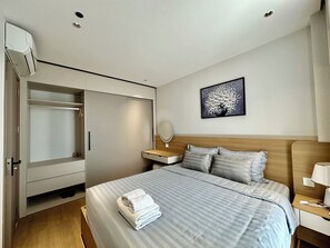 A hotel room with a bed, a bedside table, a nightstand, a wardrobe, and a wall-mounted artwork. - Spacious modern 2BR apartment Phu Quoc (Phu Quoc)