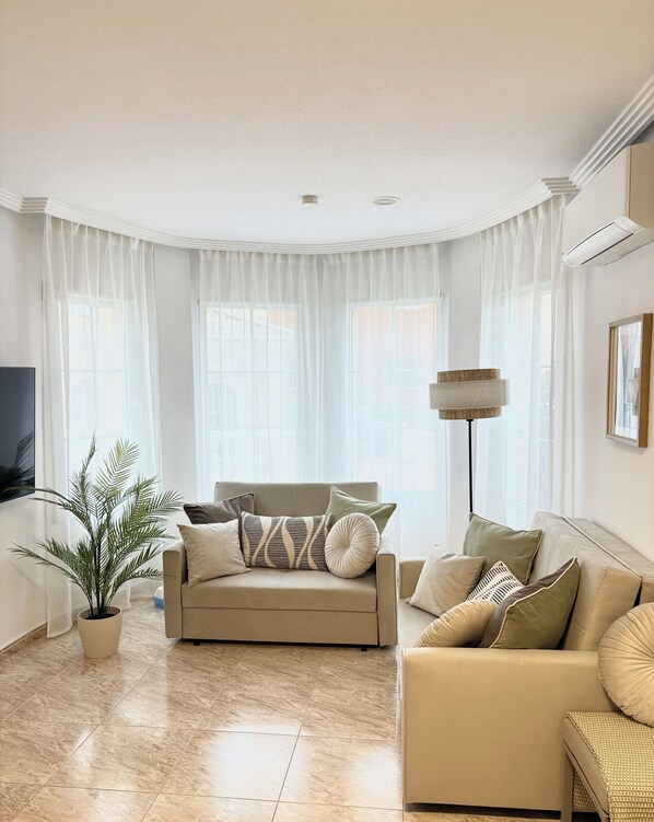A living room with a beige sofa, a floor lamp, and a television.