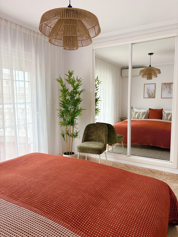 A bedroom with a large bed, a chair, a potted plant, and a view through a sliding door to another room. - Detached 3-Bed Villa with Shared Pool near La Zenia, Orihuela Costa (Orihuela)