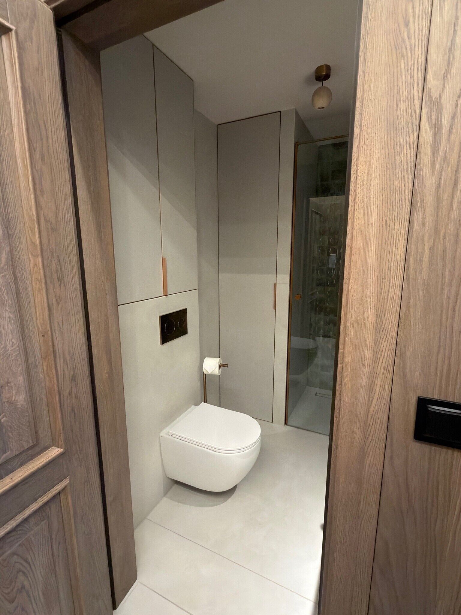 Une petite salle de bain avec des toilettes blanches, un distributeur de serviettes et une cabine de douche en verre.