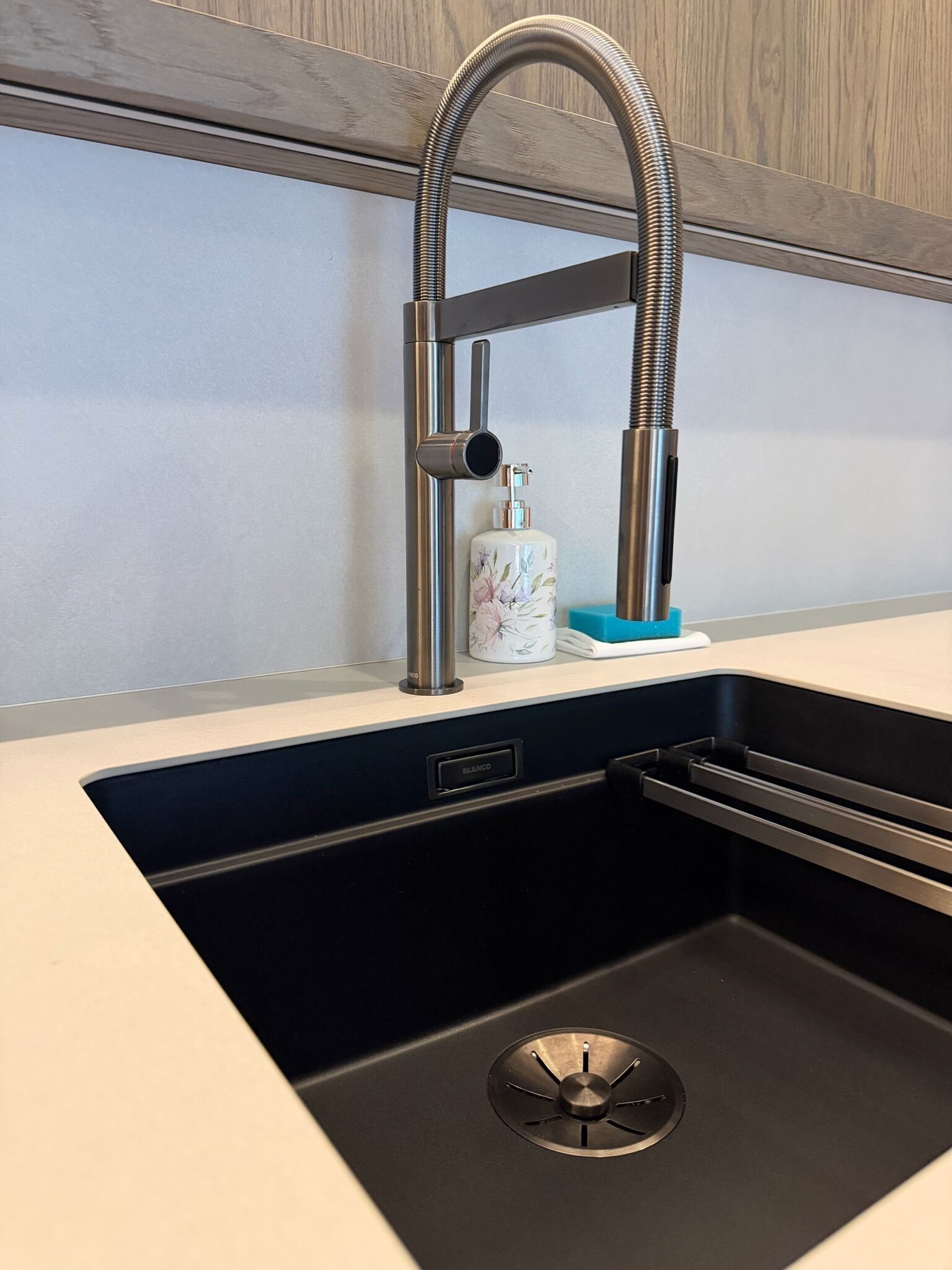 Un lavamanos de cocina con un grifo moderno, un dispensador de jabón y un protector de desagüe de acero inoxidable.