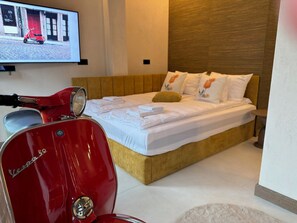 Una habitación de hotel con una cama, un scooter rojo y un televisor mostrando una escena callejera.