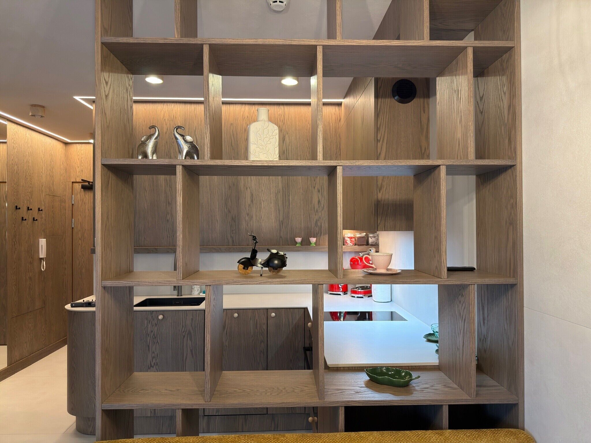 Een moderne keuken met houten kastjes, een ingebouwde vaatwasser en een eethoekje met een rode theepot en kopjes.