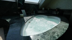 Una bañera de hidromasaje en una habitación con piso de mármol oscuro y tragaluz.