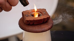 Una mano encendiendo una vela sobre un soporte de madera con base de metal.