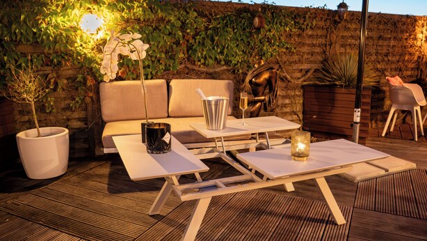 Un espacio al aire libre con sillones, dos mesas, una planta en maceta, un enfriador de champán y una vela.
