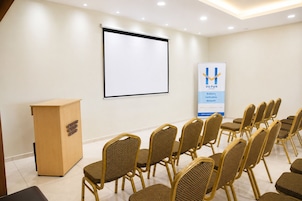 A conference room with a podium, a projection screen, and rows of wicker chairs.