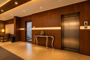 Un vestíbulo de hotel con mostrador de recepción, una silla, un ascensor y una escalera.