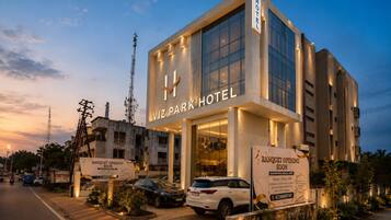 A modern hotel with a large glass facade, signage for a banquet opening, and a parking area with cars.