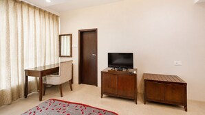Una habitación con un escritorio de madera, un televisor sobre un mueble, una puerta y una alfombra estampada.
