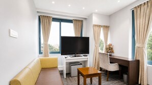 Habitación de hotel con sofá, escritorio, televisión y ventana con cortinas.