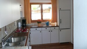 Een kleine keuken met een spoelbak, kookplaat, keukenkastjes en een raam met gordijnen.