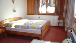 Een houten bed in een kamer met een raam, een radiator en een stoel.